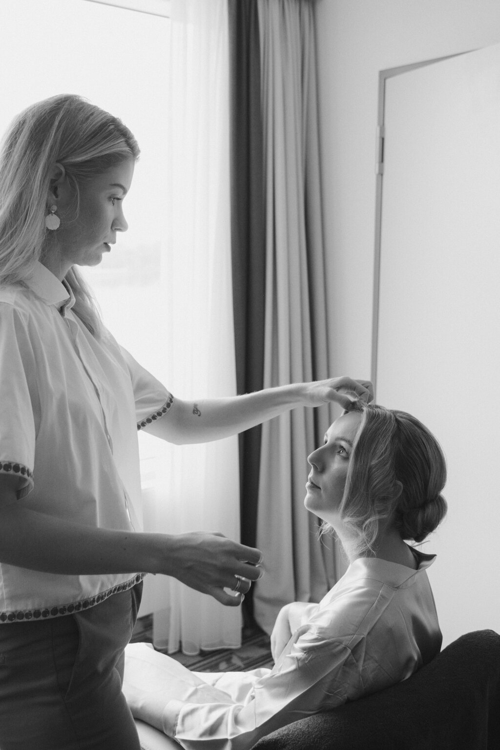 Szene aus einem getting ready in einem Hotelzimmer. Die Stylistin styled die Haare der Braut.